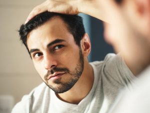 Man looking at hair in Mirror after using Hyalogic Biotin Mist